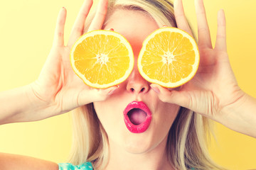 Happy young woman holding oranges halves on a yellow background