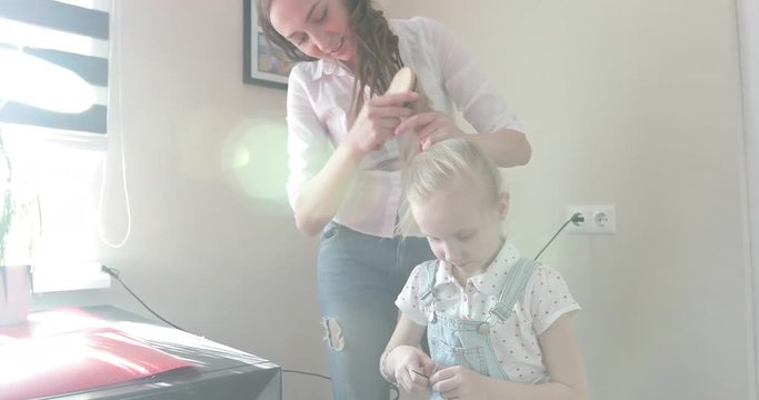Attractive mother makes her daughter hairstyle.