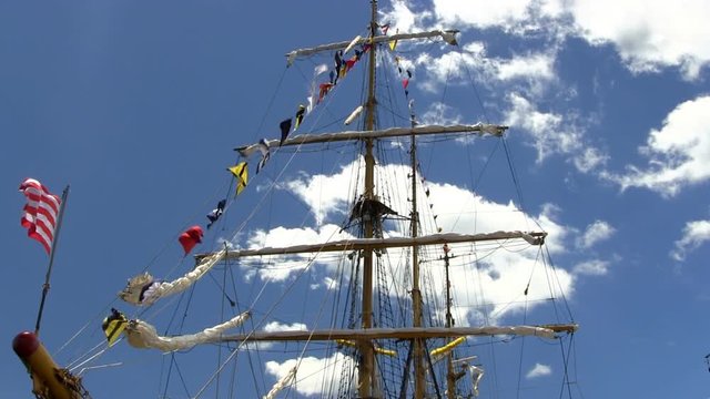 Masts, rigging, banners and flags of Indonesian tall ship Dewaruci against blue sky and clouds moving in the wind.   