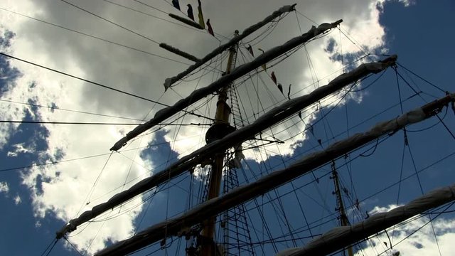 Masts, rigging, banners and flags of Indonesian tall ship Dewaruci against blue sky and dark cloud moving in the wind.   