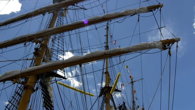 Masts, rigging, banners and flags of Indonesian tall ship Dewaruci against blue sky and clouds moving in the wind.   