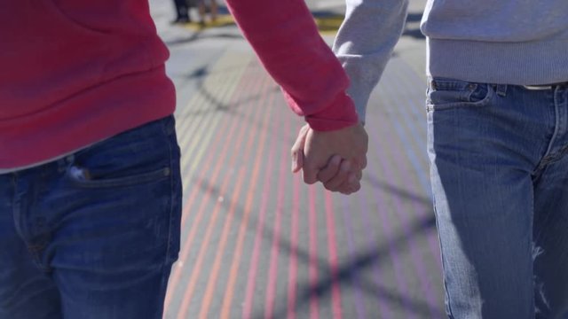 Gay Couple Hold Hands And Walk Toward Camera On Rainbow Crosswalk In San Francisco