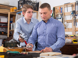  father and teen son working with wood plank in workshop
