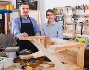 father and son chiselling a wooden bench in  workshop