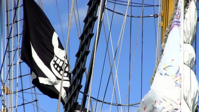 Black and white pirate flag on tall ship Dewaruci waves in wind against blue sky 