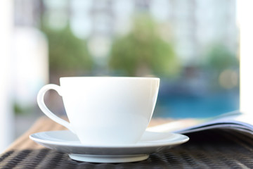 Blurred coffee cup with opened book on outdoor rattan table