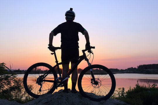 silhouette of the cyclist looking at the sunset on the pond.