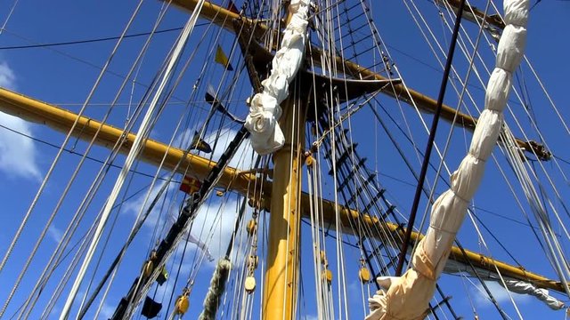 Masts, rigging, banners and flags on Indonesian tall ship Dewaruci against blue sky and clouds   