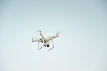 White drone hovering in a bright blue sky. Drone copter flying with digital camera
