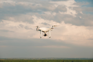 White drone hovering in a bright blue sky. Drone copter flying with digital camera
