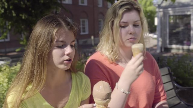 Teen Friends Sit On Bench And Enjoy Ice Cream Cones 