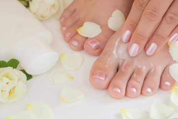 Young woman's feet with moisturizing cream. Smooth skin. Spring and summer atmosphere with fresh and fragrant white roses.