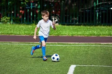 Foto op Canvas Boy football player running with ball on green lawn © Sergey Ryzhov
