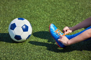 Boy football soccer tying laces him boots on grass