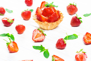 Tasty cake basket with strawberries and cream on a white wooden background with berries and leaves of fresh mint