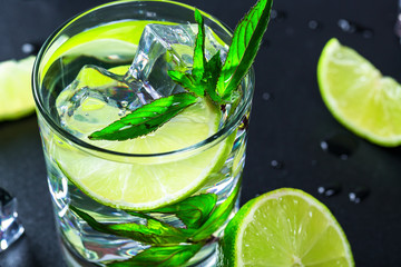 Mojito cocktail with lime, ice cubes and mint in highball glass on a black background Copy space
