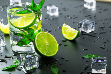 Mojito cocktail with lime, ice cubes and mint in highball glass on a black background Copy space