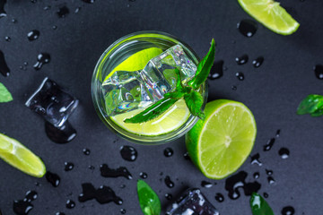 Mojito cocktail with lime, ice cubes and mint in highball glass on a black background Copy space