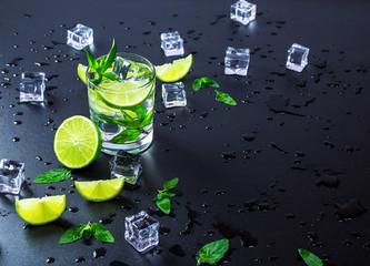 Mojito cocktail with lime, ice cubes and mint in highball glass on a black background Copy space