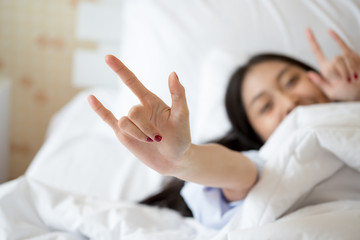 Asian girl in cozy bed with white sheets making fun hand gestures, expressing freedom, joy, and...