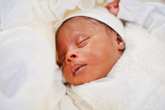 Small tiny newborn african american baby laying on the bed.