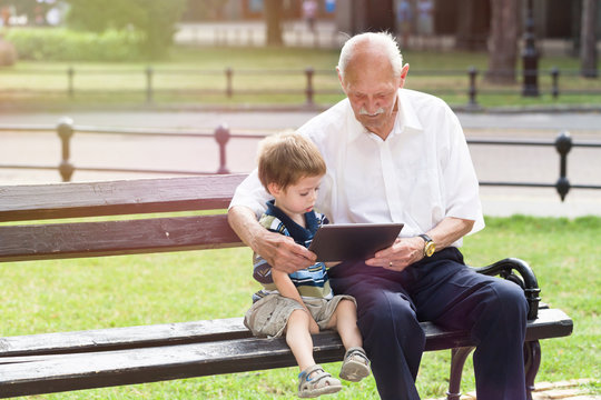 grandfather and grandson using tablet on a bench in a park in summer