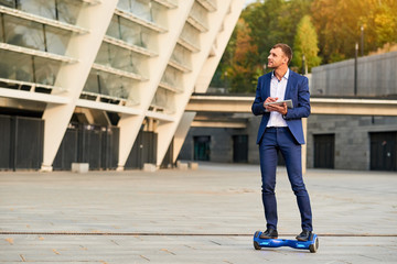 Young businessman riding hoverboard. Caucasian guy with a tablet.