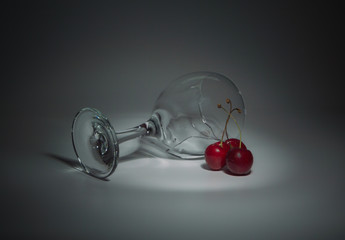 closeup of a glass with water and cherries lying on a white background.