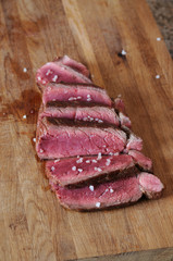Beef steak is sliced on a wooden board. Sprinkled with coarse salt
