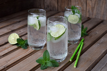 Glass of cold homemade lemonade or mojito cocktail with lime and mint on wooden background. Soda drink. Copy space.
