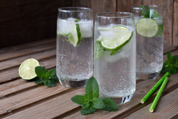 Glass of cold homemade lemonade or mojito cocktail with lime and mint on wooden background. Soda drink. Copy space.