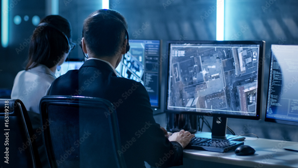 Leinwandbilder government agent is tracking fugitive with her computer in big monitoring room full of computers wit