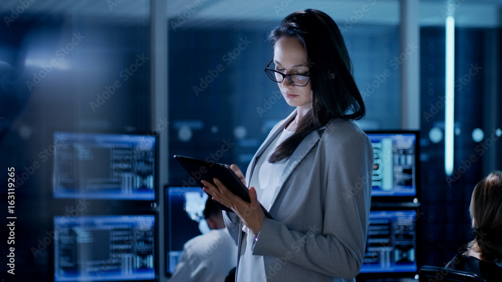 Leinwandbilder young female engineer uses tablet in system control center. in the background her coworkers are at t