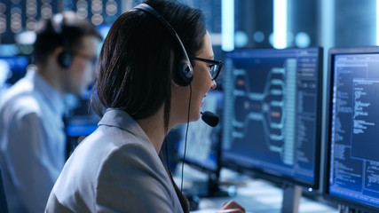 In the System Control Center Woman working in a Technical Support Team Gives Instructions with the Help of the Headsets. Possible Air Traffic/ Power Plant/ Security Room Theme. - obrazy, fototapety, plakaty