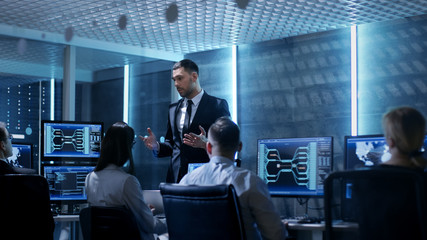 Supervisor Holds Briefing for His Employees in System Control Center Full of Monitors and Servers. Possibly Government Agency Conducts Investigation.