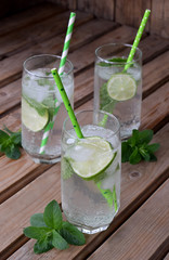 Glass of cold homemade lemonade or mojito cocktail with lime and mint on wooden background. Soda drink. Copy space.