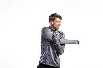 Fit man in gray sweatshirt stretching arms, studio shot.