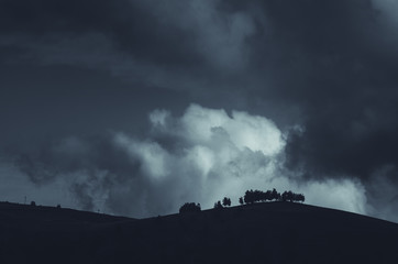 dark night landscape with cloud over tree silhouettes on hill