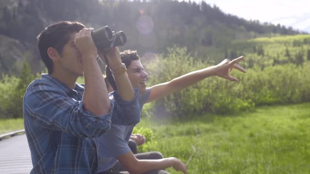 Teenage Boys Sit On A Boardwalk And Use Binoculars To Spot Wildlife (Slow Motion)