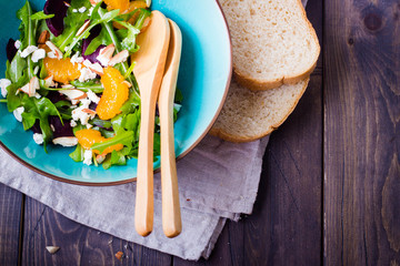 Delicious fruit and vegetables salad. Tangerine, beets, feta cheese, arugula and nut walnut in plate on wooden table background, top view with copy space. Healthy food concept.