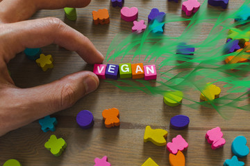 Hard strong men's hands spread the word Vegan from bright vivid alphabetic cubes, from which a fantasy grass grows, on a brown wooden table. Concept. Ready to advert