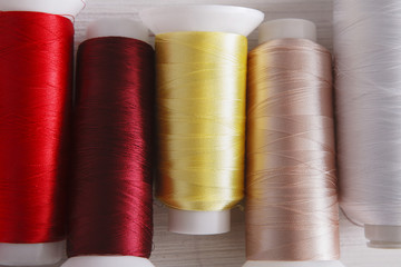 Colorful thread spools on wooden table close up