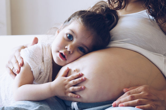 Happy kid girl hugging pregnant mother's belly