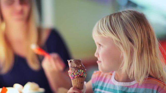 Closeup Of Little Girl As She Enjoys An Ice Cream Cone, She Looks At Her Mother And Brother And Smiles