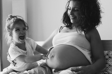 Happy kid girl with her pregnant mother on the bed