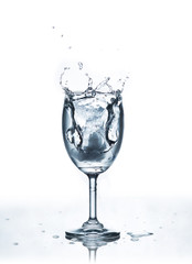Water splash with ice in glass on white