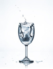 Water splash with ice in glass on white