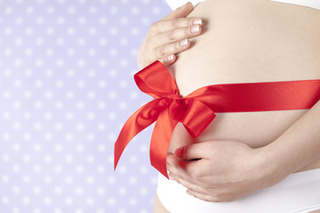 Pregnant woman belly with red ribbon gift