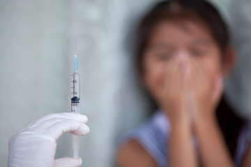 Close up doctor hand holding syringe with a child girl fear to receive vaccine injection background
