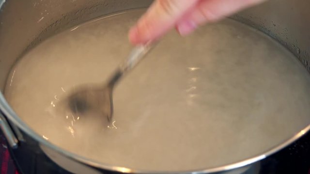 A woman stirs water with gelatin powder in a steel bowl - closeup